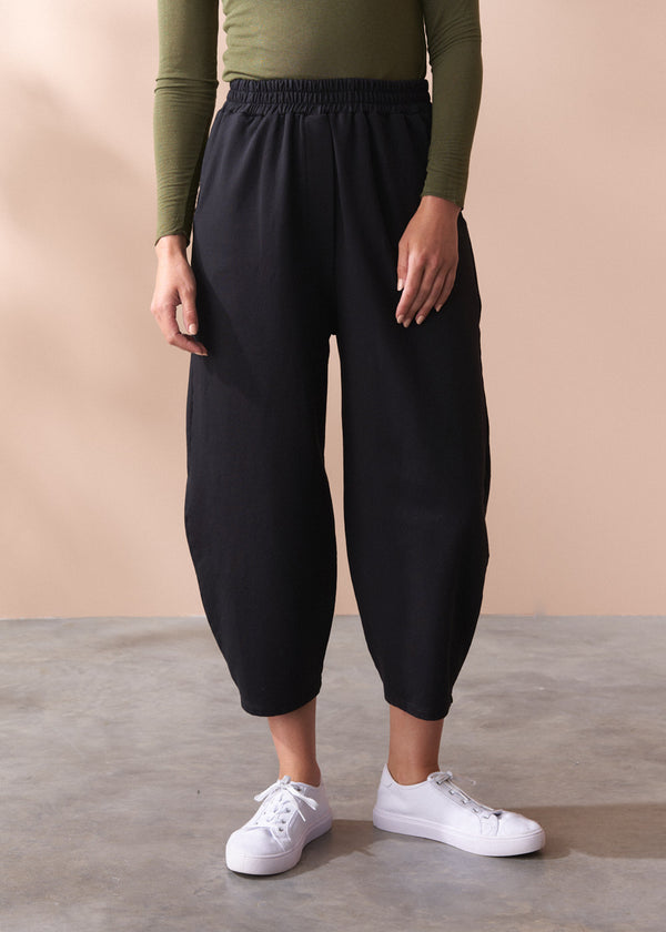 Person wearing black barrel leg cotton trousers and white sneakers on a beige background