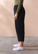 Person wearing black barrel leg cotton trousers and white sneakers on a beige background