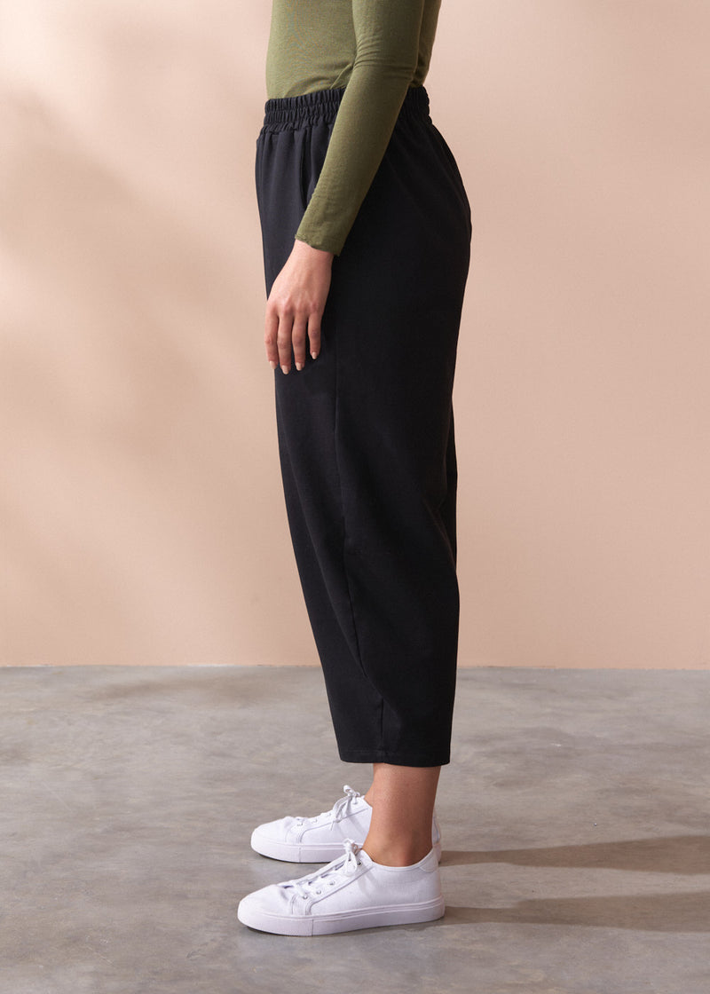 Person wearing black barrel leg cotton trousers and white sneakers on a beige background