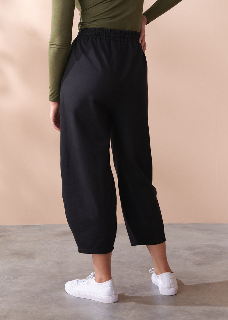 Person wearing black barrel leg cotton trousers and white sneakers on a beige background