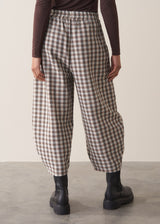 Woman wearing a brown poloneck sweater and checked barrel leg trousers against a plain background