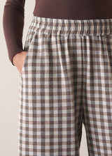 Woman wearing a brown poloneck sweater and checked barrel leg trousers against a plain background