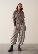 Woman wearing a brown poloneck sweater and checked barrel leg trousers against a plain background