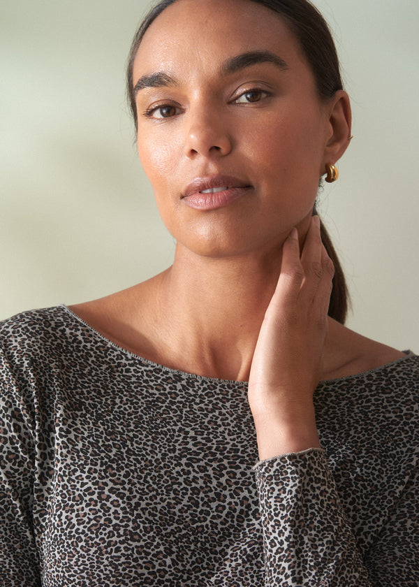 Woman wearing a grey leopard print top with dark jeans against a plain background