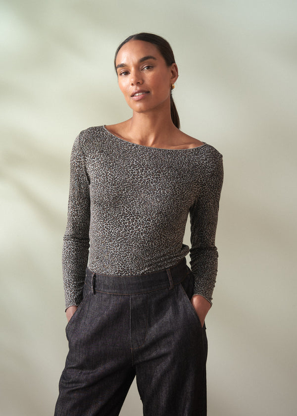 Woman wearing a grey leopard print top with dark jeans against a plain background