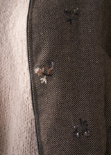 Person wearing a brown textured bomber jacket with sequin detail and black trousers on a plain background