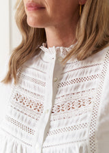 Close-up of a woman wearing a white embroidered blouse with eyelet lace panels and a ruffled high neck.
