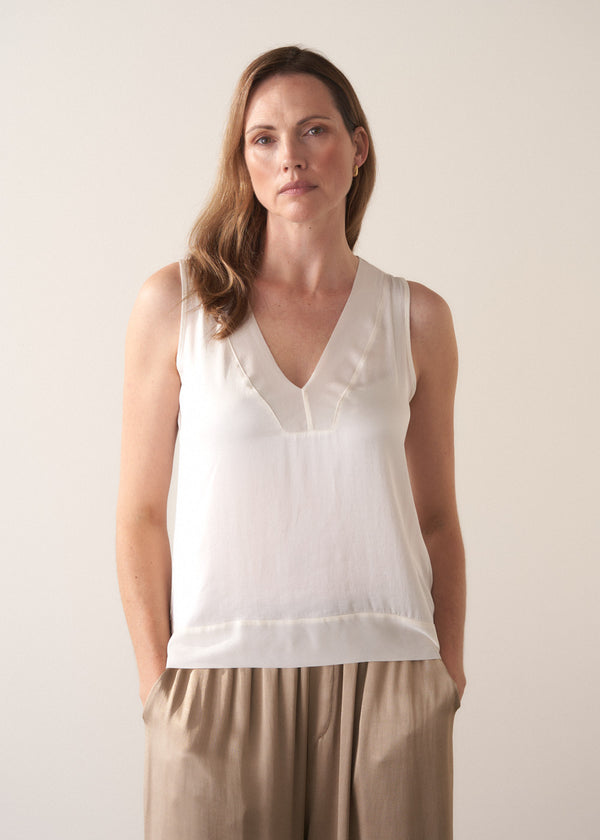 Woman wearing a white sleeveless top and gold satin trousers against a plain background