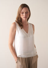Woman wearing a white sleeveless top and gold satin trousers against a plain background