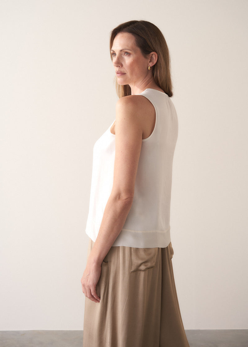 Woman wearing a white sleeveless top and gold satin trousers  against a plain background