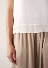 Person wearing a white top and gold satin trousers  against a plain background