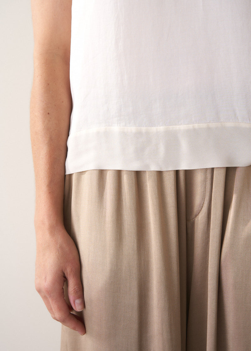 Person wearing a white top and gold satin trousers  against a plain background