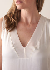 Close-up of a person wearing a white sleeveless top with a plain background