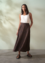 Woman wearing a white top and leopard print brown skirt against a plain background