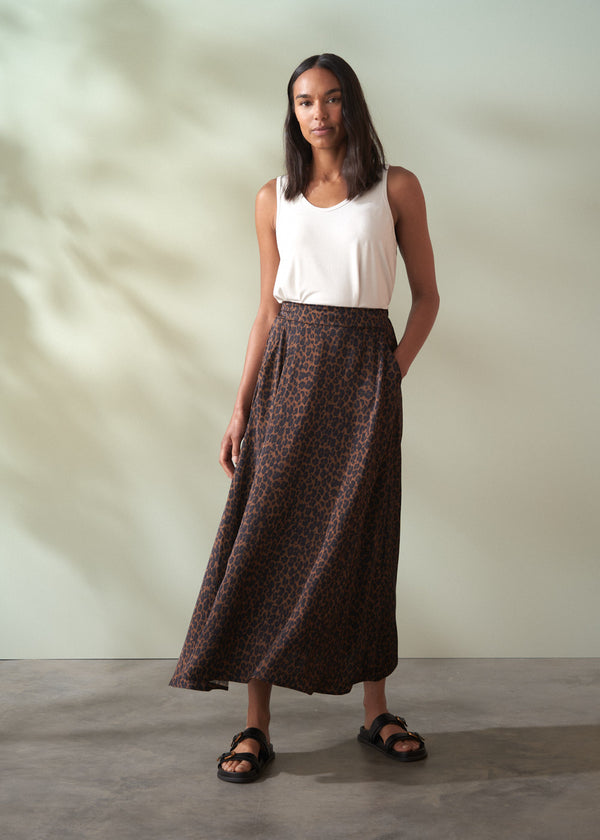 Woman wearing a white top and leopard print brown skirt against a plain background
