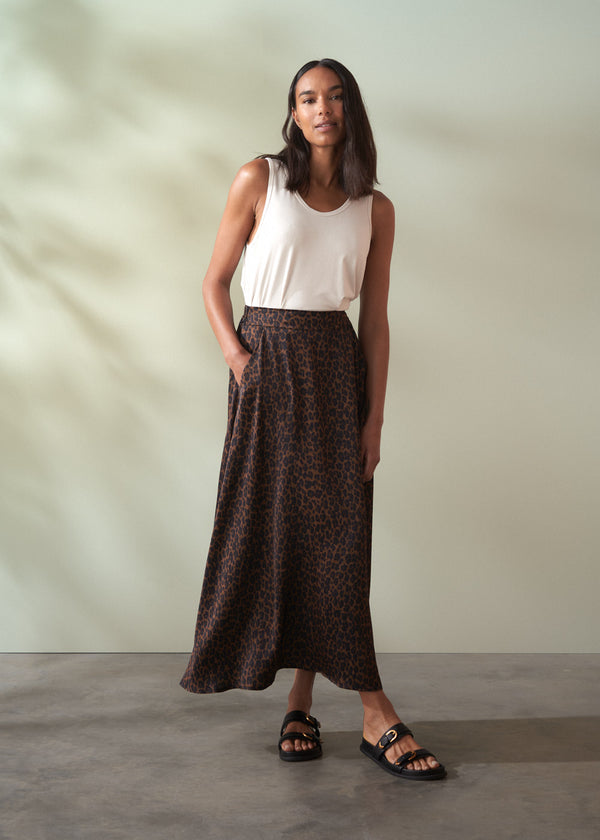 Woman wearing a white top and brown patterned skirt against a plain background