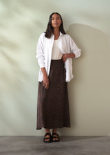 Woman wearing a white shirt and leopard print skirt against a plain background