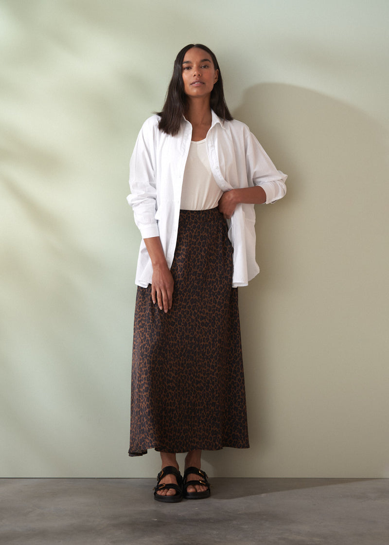 Woman wearing a white shirt and leopard print skirt against a plain background
