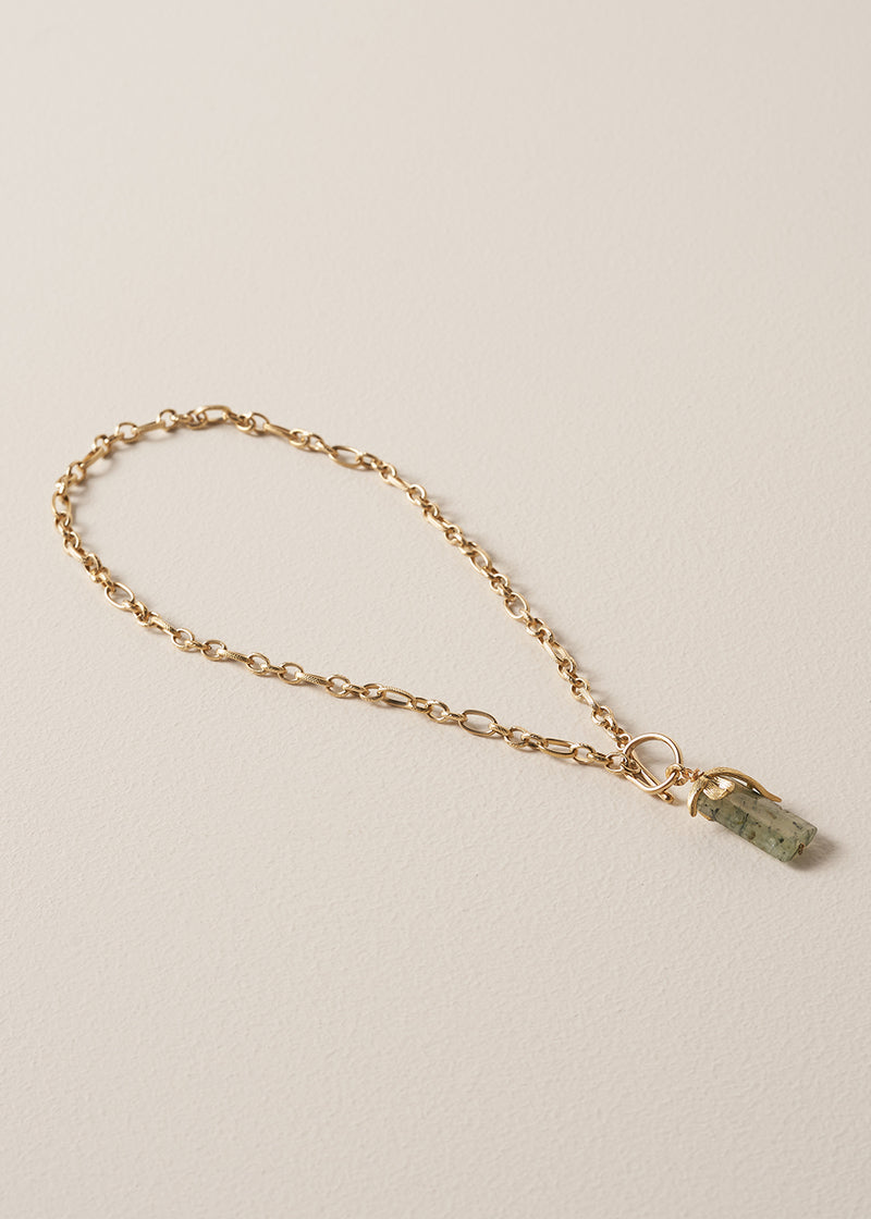 Gold chunky chain necklace with a green stone pendant on a beige background