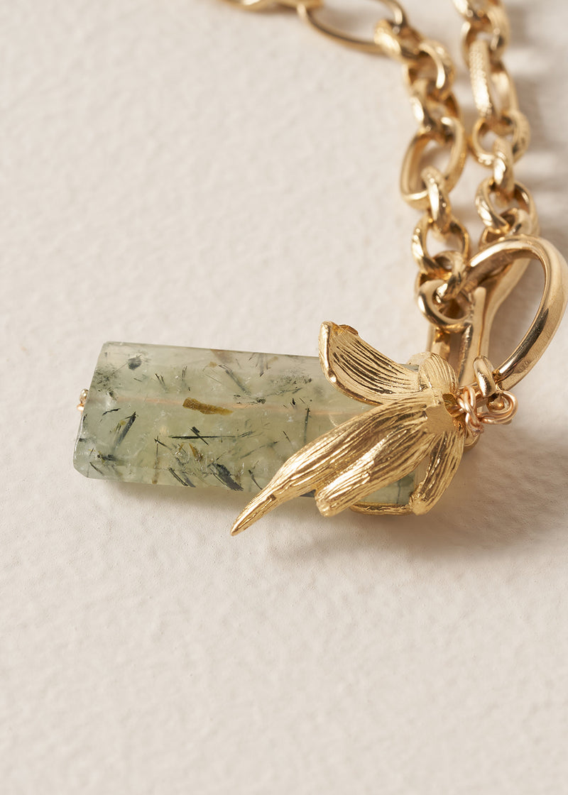 Gold chunky chain necklace with a green stone pendant on a beige background