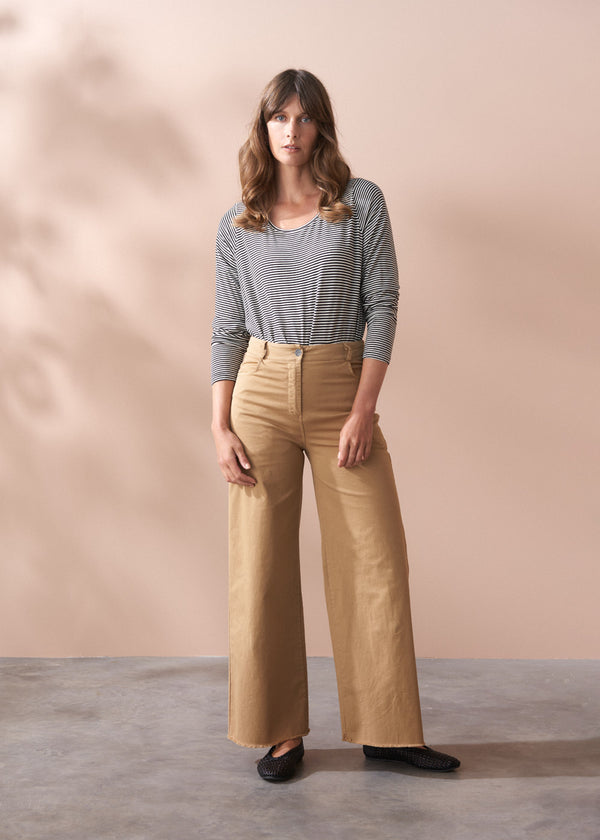 Person wearing beige wide-leg trousers and a striped long sleeve top against a plain background