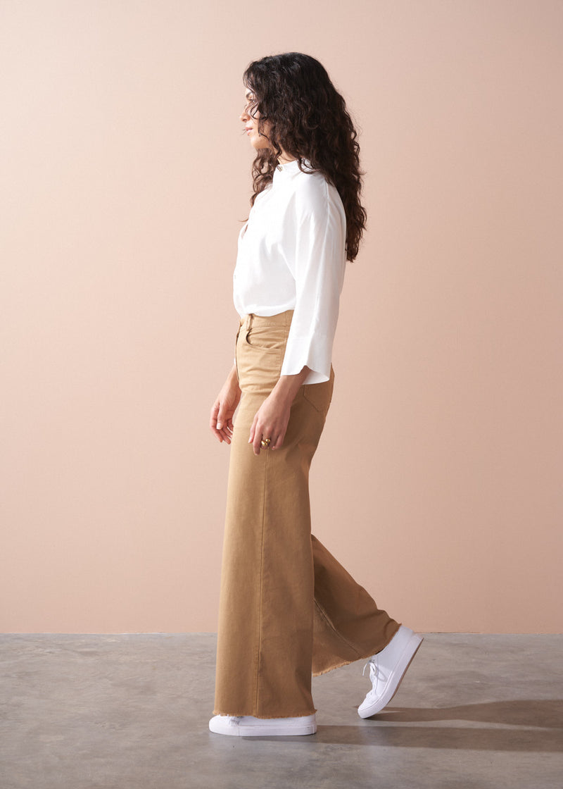 Woman wearing a white blouse and tan wide-leg pants against a beige background