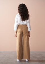 Woman wearing a white blouse and tan wide-leg pants against a beige wall.