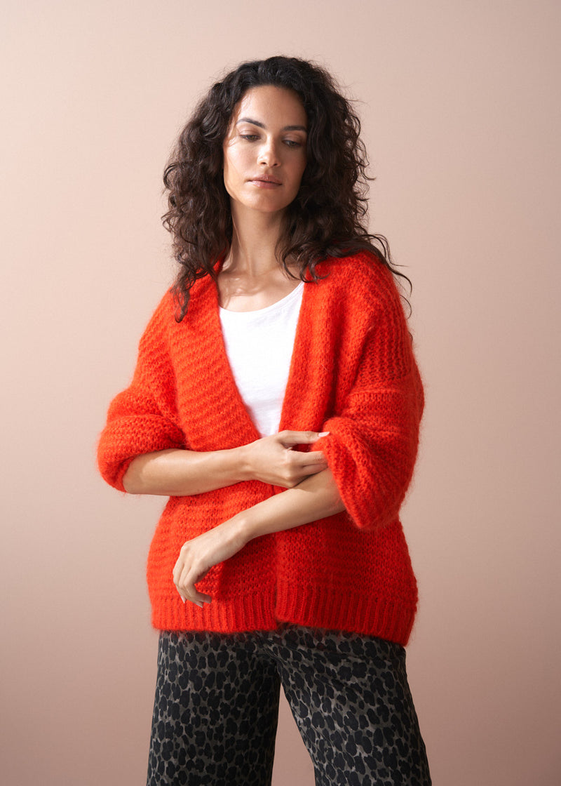 Woman wearing a bright red cardigan over a white shirt on a beige background