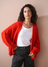 Woman wearing a red cardigan over a white shirt and leopard print trousers against a beige background
