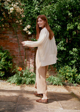 Woman wearing a white striped shirt and beige wide leg trousers in a garden