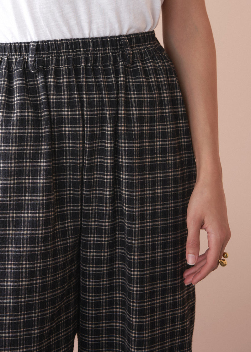 Plaid barrel leg trousers worn by a person on a beige background