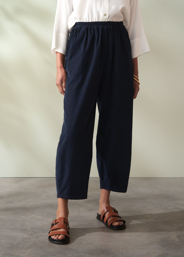 Person wearing navy corduroy barrel leg trousers and brown sandals on a plain background