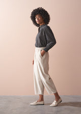 Woman wearing a check shirt and beige corduroy barrel leg trousers against a beige background