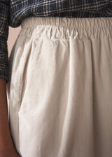 Woman wearing a check shirt and beige corduroy barrel leg trousers against a beige background