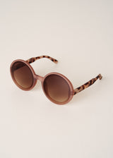 Round sunglasses with brown lenses and tortoiseshell arms on a light beige background