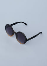 A pair of chunky circular sunglasses with black and pink frames and blue lenses