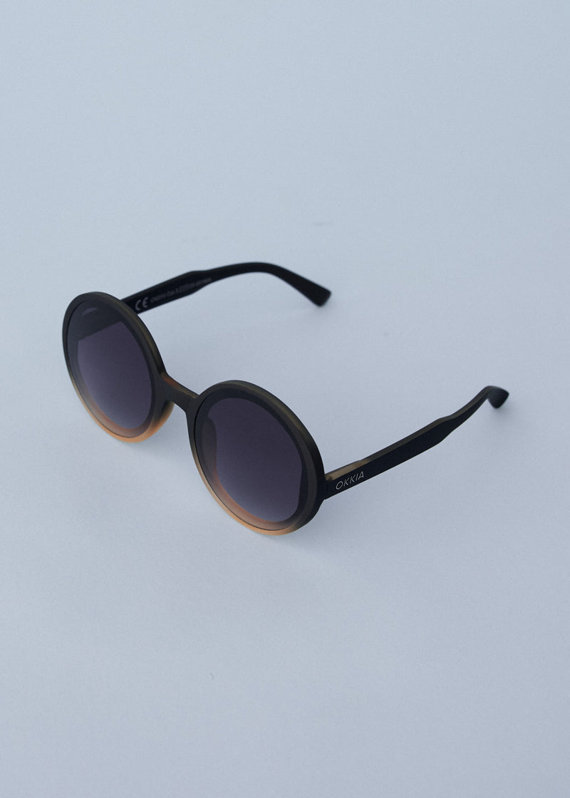 A pair of chunky circular sunglasses with black and pink frames and blue lenses