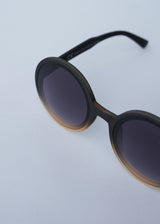 A pair of chunky circular sunglasses with black and pink frames and blue lenses