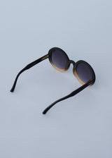 A pair of chunky circular sunglasses with black and pink frames and blue lenses