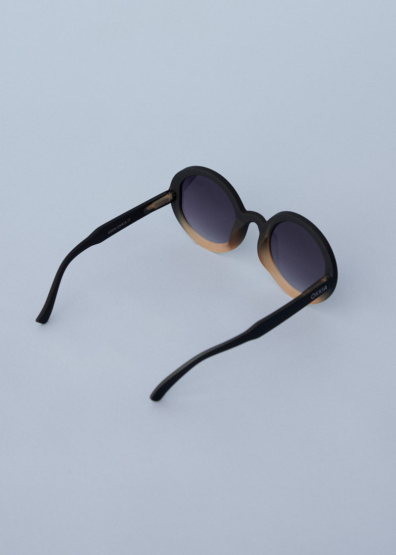 A pair of chunky circular sunglasses with black and pink frames and blue lenses