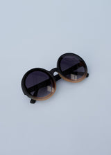 A pair of chunky circular sunglasses with black and pink frames and blue lenses