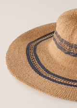 Close up of oversized straw sunhat with black stripe pattern against a beige background
