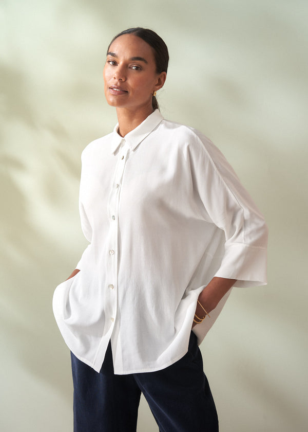 Woman wearing a white shirt and navy trousers against a plain background