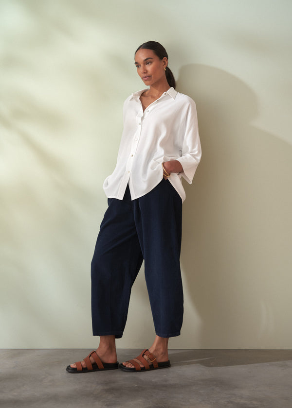 Woman wearing a white shirt and navy trousers against a plain background