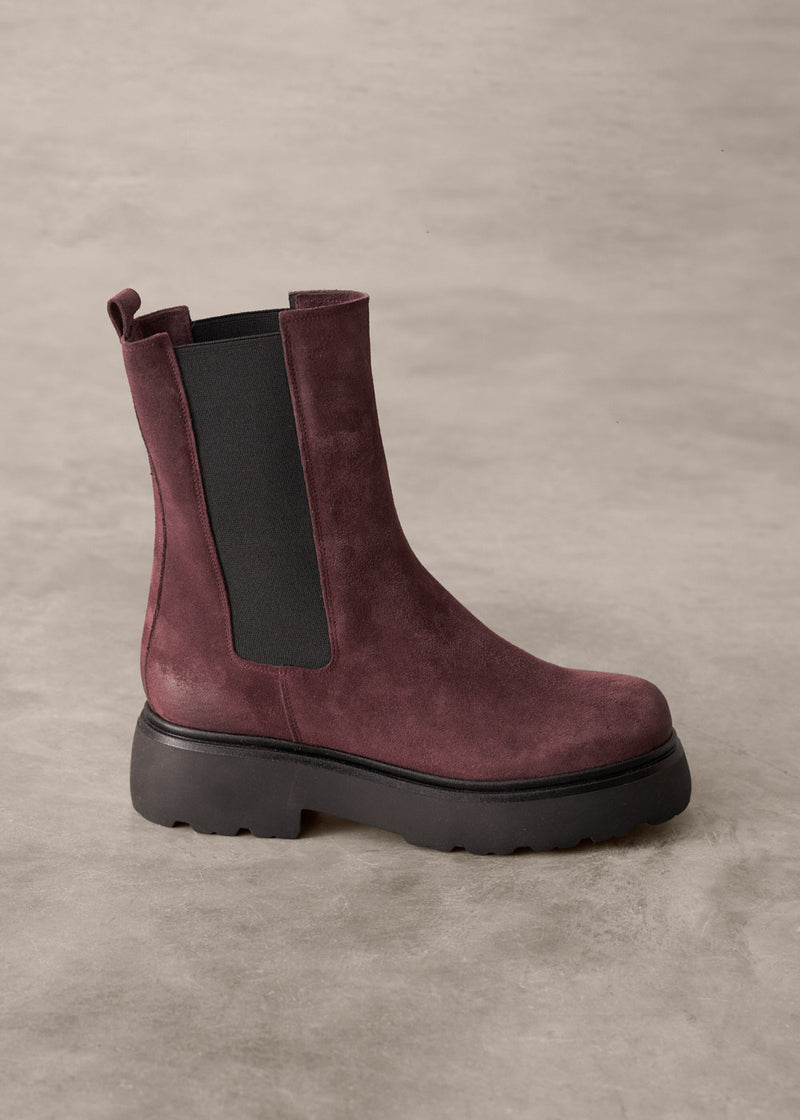 Burgundy suede boot with black sole on a gray background