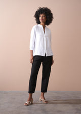 Woman wearing a white shirt and black trousers against a beige background