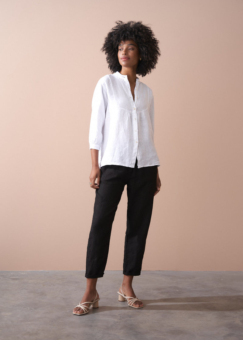 Woman wearing a white shirt and black trousers against a beige background
