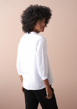Woman wearing a white shirt and black trousers against a beige background