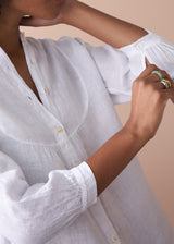 Person wearing a white shirt with rolled-up sleeves against a beige background