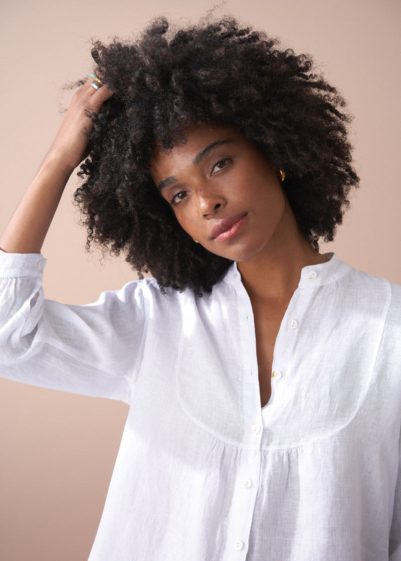 Woman with natural hair wearing a white shirt against a beige background